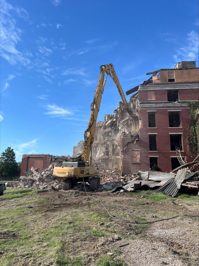 Komatsu excavator demolishing brick building on clear day