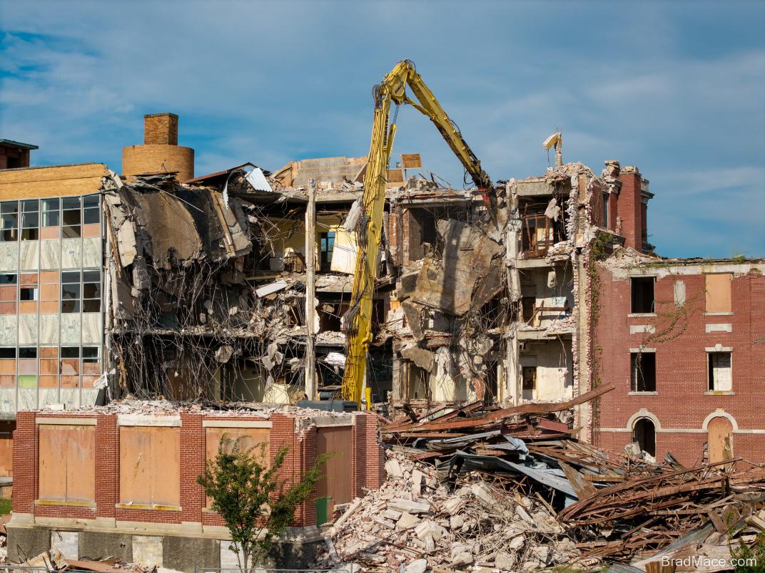 Excavator demolishing multi-story brick building